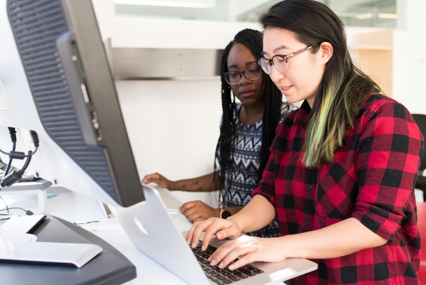 Two women collaborating on a project at a computer workstation, representing teamwork in understanding what an ERP system is and how it supports business operations.