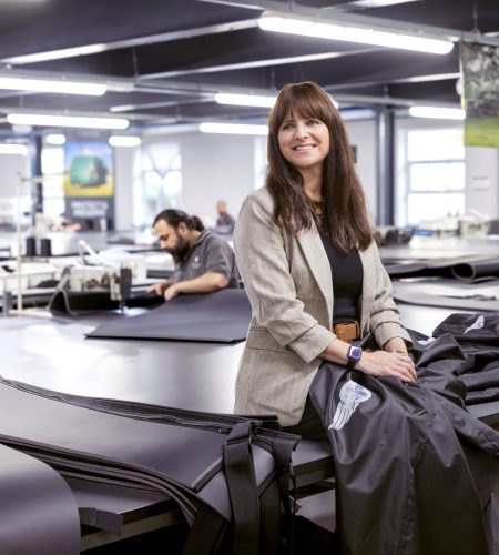 Katie Fishwick, MD at Specialised Covers, sitting in the manufacturing warehouse with skilled workers creating covers.